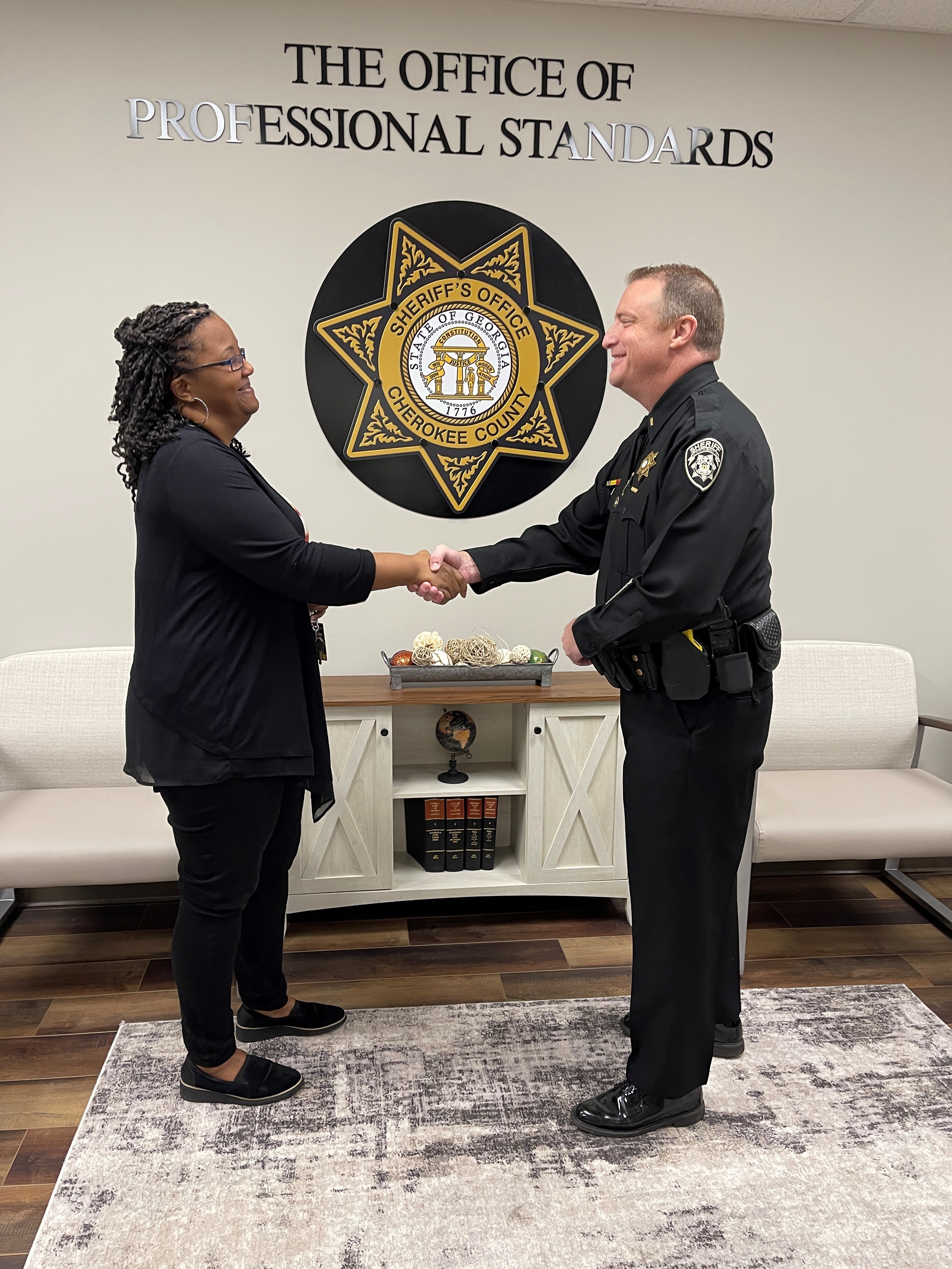 Raquel Hemby and Lt. David Barone shaking hands in front of a sign that says 'The Office of Professional Standards'.
